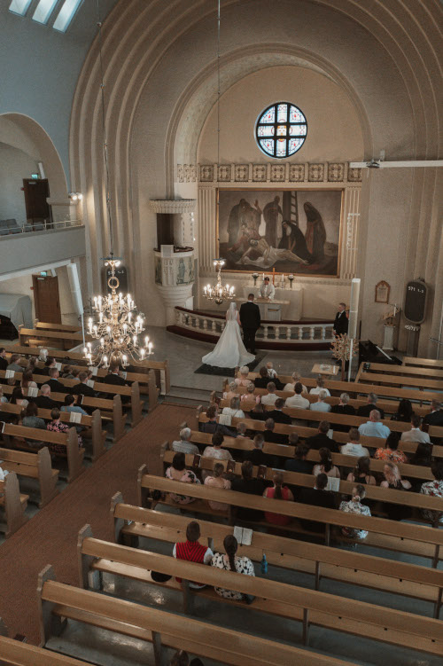 Kirkko vihkitilanne kuvattuna niin, että alttari näkyy sekä häävieraat kirkonpenkeillä.